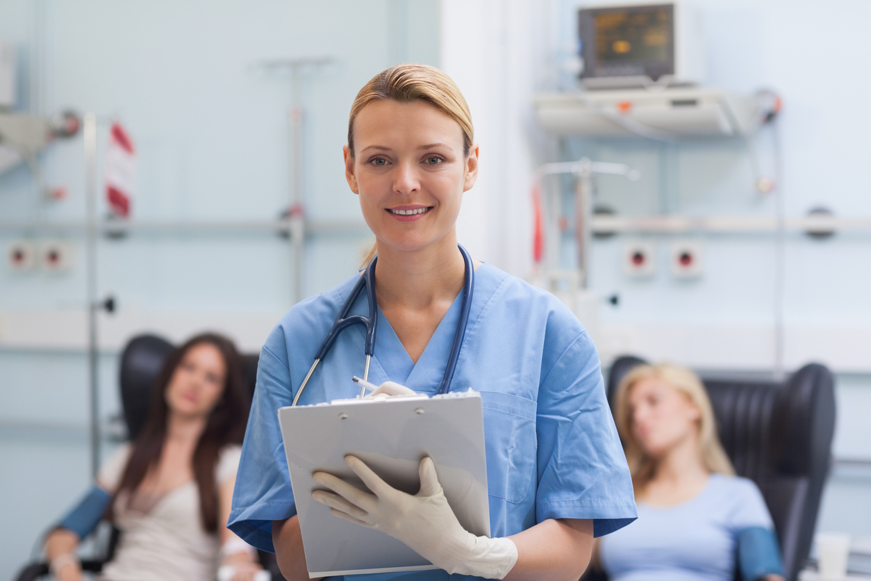 Nurse writing on a clipboard next to patients in hospital ward